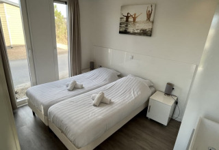 Chambre moderne en lodge avec deux lits simples, linge blanc, table de chevet et grande fenêtre vitrée.