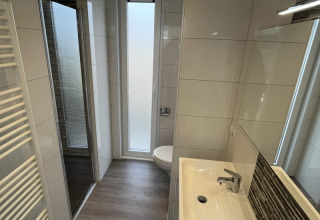Un moderno baño de lodge con ducha, lavabo, inodoro y ventanas altas opacas para mayor privacidad.