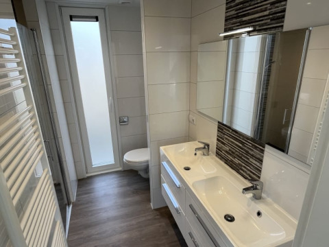 Salle de bain moderne dans un lodge avec double vasque, miroirs, toilettes et grande fenêtre mate.