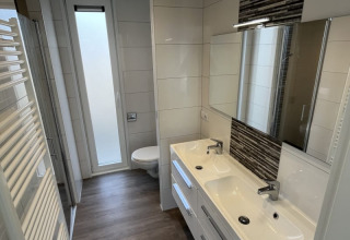 Baño moderno de lodge con dos lavabos, espejos, inodoro y una ventana alta esmerilada.