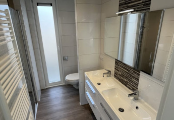 Baño moderno de lodge con dos lavabos, espejos, inodoro y una ventana alta esmerilada.