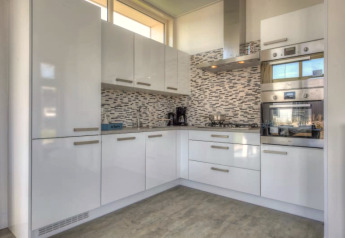 Modern kitchen in a lodge featuring white glossy cabinets, built-in oven, gas stove, and tiled backsplash.