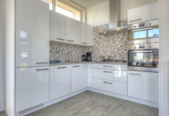 Cucina moderna in un lodge con mobili bianchi lucidi, forno a incasso, piano cottura e piastrelle decorative.
