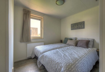 Bright bedroom in a lodge featuring two single beds with gray bedding, a window, and wall art above.