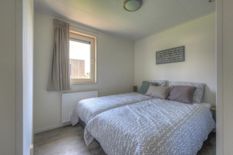 Dormitorio luminoso en una cabaña con dos camas individuales, ropa de cama gris, ventana y cuadro mural.