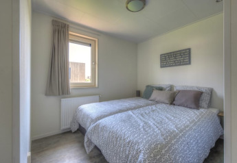 Dormitorio luminoso en una cabaña con dos camas individuales, ropa de cama gris, ventana y cuadro mural.