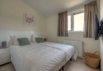 Bright modern lodge bedroom with two single beds, green pillows, wall art, wicker basket, and TV on wall.