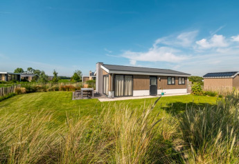 Lodge moderne avec grande pelouse, terrasse extérieure et ciel bleu, entouré de verdure et nature.