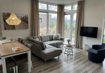 Salon de lodge moderne avec canapé d’angle, table à manger, TV écran plat, grandes fenêtres et déco bois.