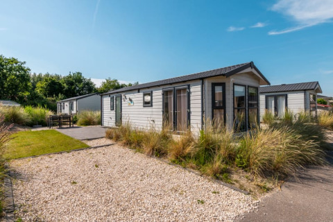 Photo of a modern lodge with gravel path, greenery, and bright sunshine beneath a clear blue sky.