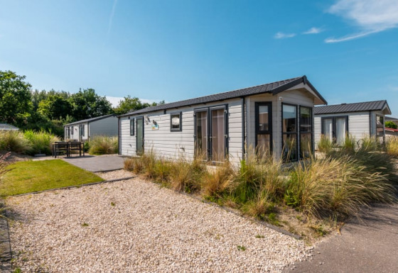 Photo of a modern lodge with gravel path, greenery, and bright sunshine beneath a clear blue sky.