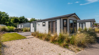 Photo d’un lodge moderne avec chemin de gravier, espaces verts et soleil sous un ciel bleu éclatant.