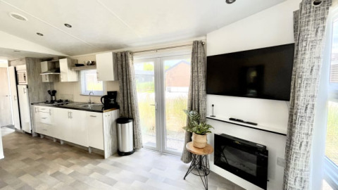 Modern lodge interior with open kitchen, wall-mounted TV, fireplace, large windows, and trendy décor.