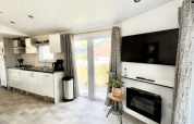 Intérieur de lodge moderne avec cuisine ouverte, TV murale, cheminée, grandes fenêtres et déco soignée.