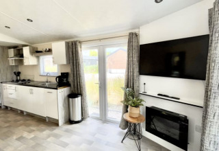 Intérieur de lodge moderne avec cuisine ouverte, TV murale, cheminée, grandes fenêtres et déco soignée.