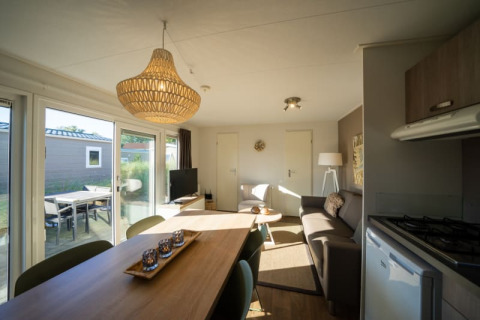 Moderne Lodge-Wohnzimmer mit Esstisch, Sofa, Küchenzeile und großen Fenstern zur Terrasse hin.