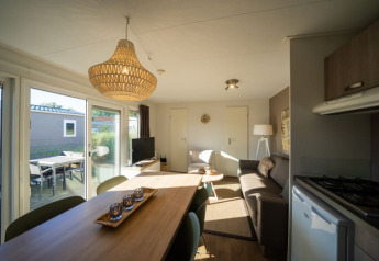 Sala de estar de lodge moderna con mesa de comedor, sofá, cocina pequeña y grandes ventanas a la terraza.