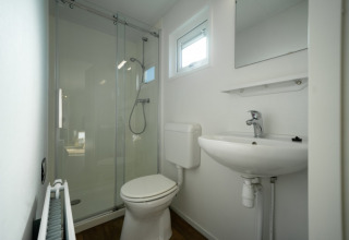 Un baño moderno y compacto en una cabaña con ducha de vidrio, inodoro, lavabo, espejo y ventana.