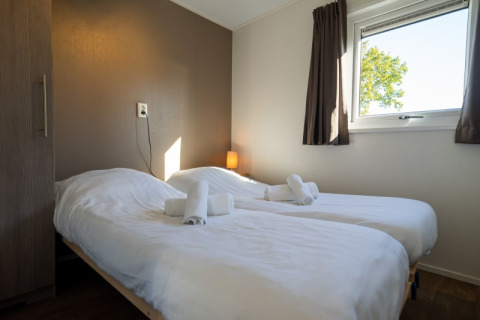 Bright lodge room with two single beds, clean white linens, towels, a window, and brown curtains.