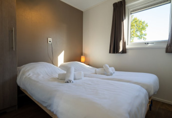 Helles Lodge-Zimmer mit zwei Einzelbetten, weißen Laken, Handtüchern, Fenster und braunen Vorhängen.