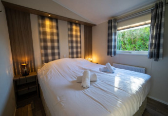 Dormitorio acogedor de una cabaña con cama doble, cortinas a cuadros y ventana con vistas a la naturaleza.