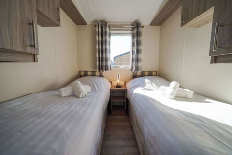 Lodge room featuring two single beds, white linens, wooden cabinets, a small window, and plaid curtains.