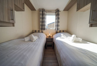 Lodge room featuring two single beds, white linens, wooden cabinets, a small window, and plaid curtains.