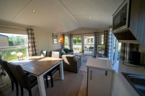 Modern lodge interior with dining table, sofa, kitchenette and large windows offering scenic views.