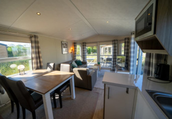 Intérieur de lodge moderne avec table à manger, canapé, coin cuisine et grandes fenêtres sur la nature.