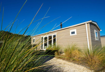 Lodge moderne aux grandes fenêtres, entouré de hautes herbes sous un ciel bleu éclatant.