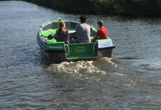 Tre persone viaggiano su una piccola barca verde chiamata Greenjoy lungo un canale vicino a Loënga, in Frisia.