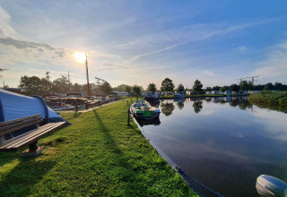 Solrig morgen ved Camping Pasveer i Friesland, Nederlandene, med både, græs og spejlblankt vand.