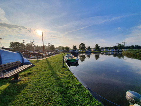 Sonniger Morgen am Camping Pasveer in Friesland, Niederlande, mit Booten am Wasser und Wohnwagen.