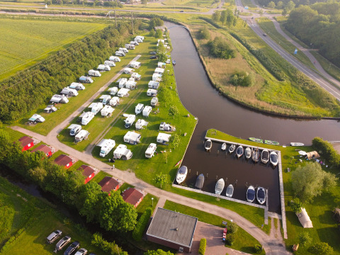 Vista aerea del Camping Pasveer in Frisia, Paesi Bassi, con camper, bungalow e barche ormeggiate al molo.