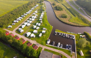 Vista aerea del Camping Pasveer in Frisia, Paesi Bassi, con camper, bungalow e barche ormeggiate al molo.