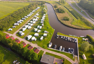 Vue aérienne du Camping Pasveer en Frise, Pays-Bas, avec camping-cars, chalets et bateaux amarrés au port.