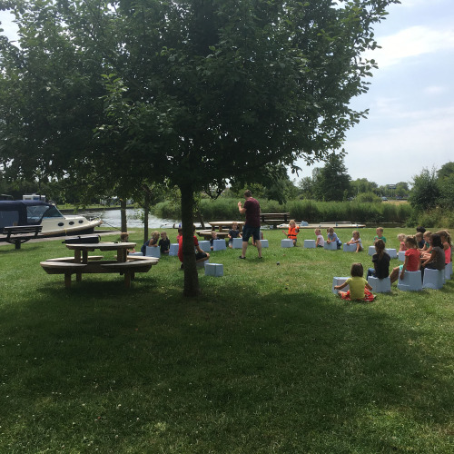 Kinder sitzen draußen bei Camping Pasveer in Friesland, Niederlande, nahe einem Boot und Bäumen.