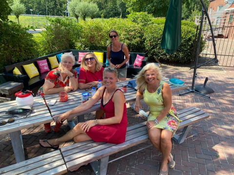 Cinque donne sorridono sedute a un tavolo da picnic al Camping Pasveer in Frisia, Paesi Bassi, in una giornata soleggiata.
