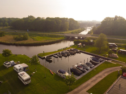 Aerial view of Camping Pasveer in Friesland, Netherlands showing boats, campers, and lush green scenery.
