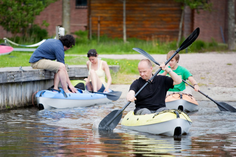 Quattro persone fanno kayak vicino alla riva al Camping Pasveer a Friesland, Paesi Bassi, in una giornata estiva.