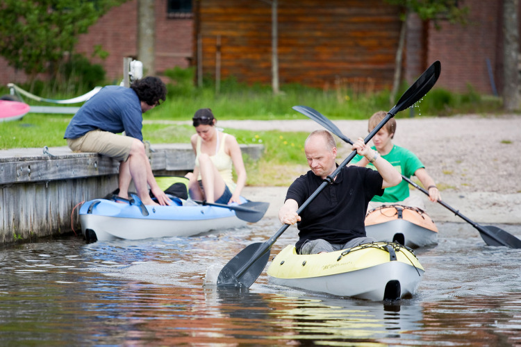 Vier Menschen paddeln in Kajaks am Ufer des Camping Pasveer in Friesland, Niederlande, im Sommer.