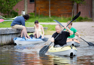 Four people kayak near the shore at Camping Pasveer holiday park in Friesland, Netherlands on a summer day.