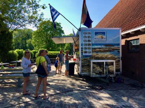 Personas esperando en un camión de comida con bandera griega en Camping Pasveer, Friesland, Países Bajos.