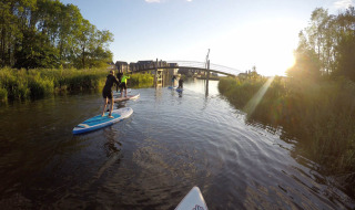 Personas haciendo paddle surf en un canal cerca de Camping Pasveer en Friesland, Países Bajos, al atardecer.