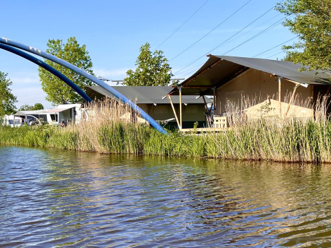Vista a través del agua hacia tiendas y casas rodantes en Camping Pasveer, parque vacacional en Frisia, Países Bajos.