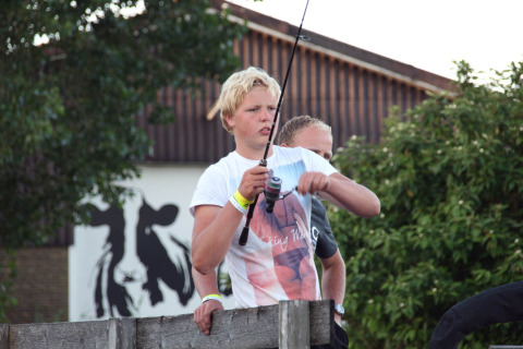 Giovane che pesca al Camping Pasveer, Friesland, Paesi Bassi, con immagine di mucca sullo sfondo.
