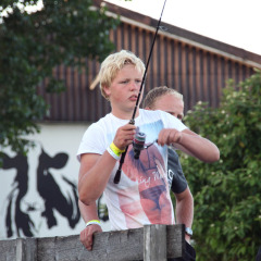 Joven pescando en Camping Pasveer, Friesland, Países Bajos, con una imagen de vaca de fondo.