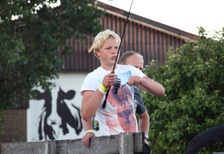 Ung fyr fisker på Camping Pasveer i Friesland, Holland, med en sort-hvid ko på væggen bagved.