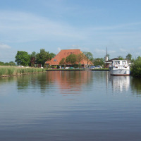 Un barco navega por un canal tranquilo cerca de Loënga, Frisia, Países Bajos, junto a una casa al fondo.