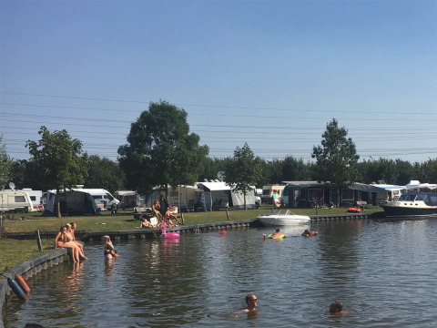 Campingplatz am See in Friesland, Niederlande, mit Menschen im Wasser, Wohnwagen und Booten im Sommer.